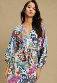 Ziedu raksta wraps kleita no viegla auduma ar spilgtām krāsām, tostarp zilu, rozā, sarkanu un zaļu, ar garām piedurknēm un jostu viduklī.