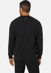Sweat à capuche noir avec manches longues, col rond et poignets côtelés. Présente un petit logo à l'arrière. Tissu doux et texturé.