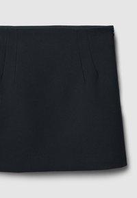 Jupe noire avec une texture lisse, dotée de deux plis à l'avant et d'une coupe droite. Fermeture éclair à l'arrière. Design simple et minimal.