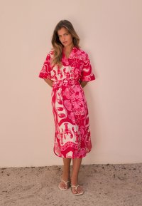 Robe rose à motifs avec ceinture nouée, manches courtes, présentant des dessins audacieux représentant la vie marine. Tissu lisse et longueur au genou.