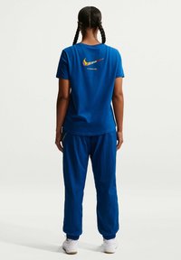 Blå bomulls-T-shirt med en färgglad Nike-logga och texten "FC BARCELONA" på ryggen, kombinerad med matchande blå byxor och vita sneakers.