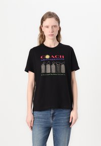 Camiseta de algodón negra con texto "COACH LEATHERWARE" y gráficos coloridos en la parte frontal, corte relajado, mangas cortas.