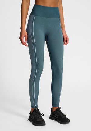 Teal sportleggings met een hoge tailleband, geribbelde textuur en witte verticale strepen aan de zijkanten. Gecombineerd met zwarte sportschoenen.
