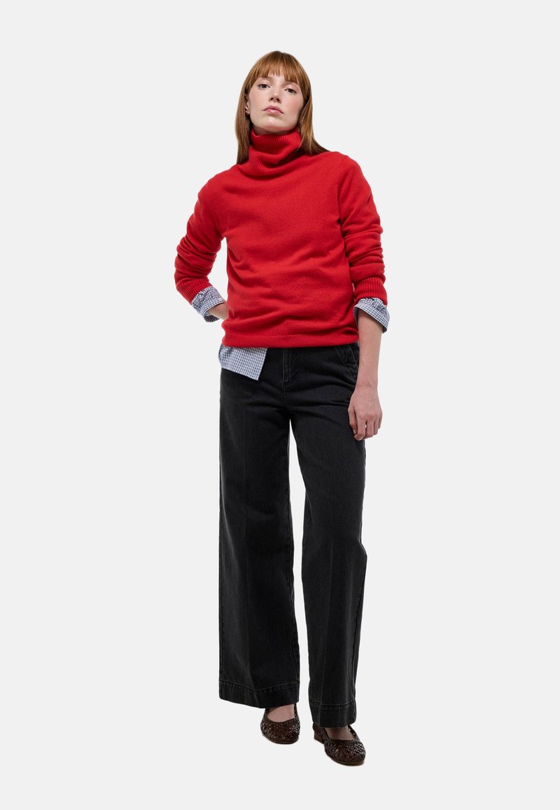 Pull à col roulé rouge en matériau doux, assorti à un jean noir à jambes larges. Présente un col de chemise à carreaux bleu clair.
