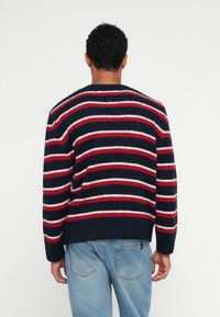 Jersey a rayas en colores marino, rojo y blanco, con puños y dobladillo acanalados, que presenta un corte holgado y un diseño de punto texturizado.