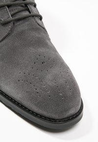 Gray suede men's dress shoe with perforated decorative pattern and rounded toe on flat black sole.