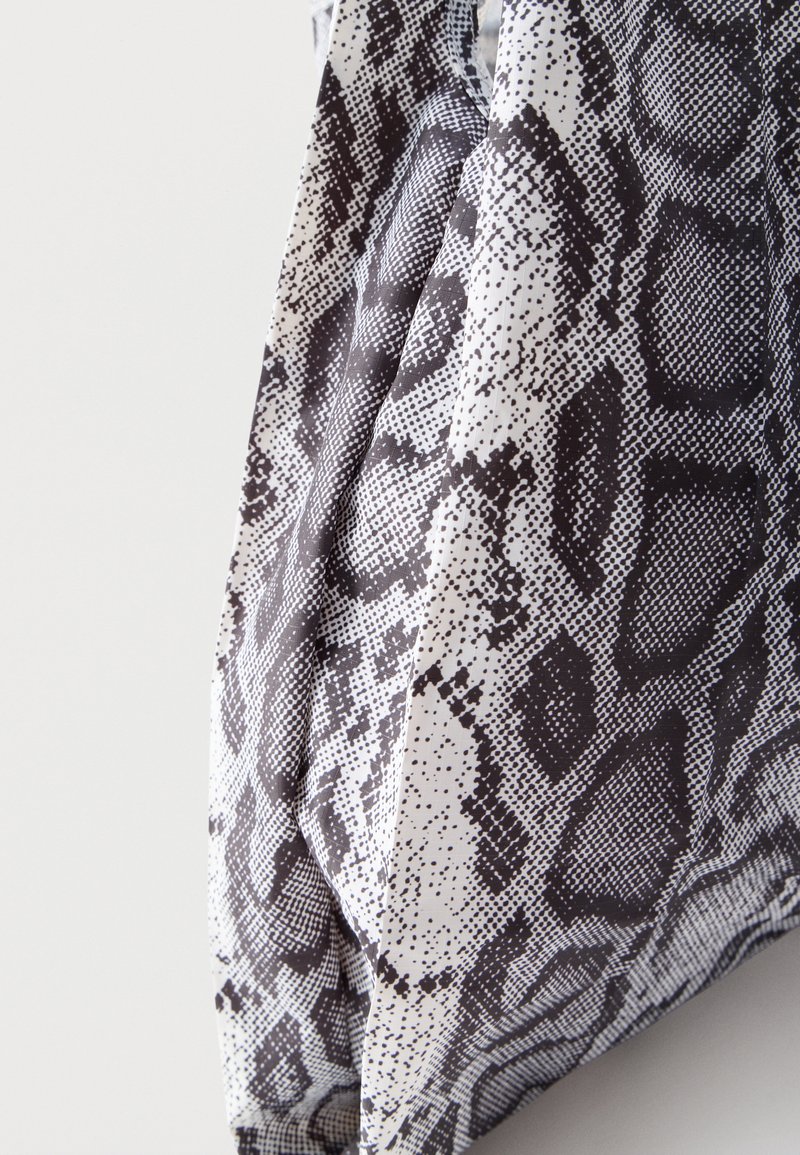 Tissu avec motif peau de serpent en noir et blanc, présentant des écailles texturées et des plis superposés sur un fond clair uni.