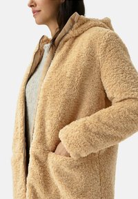 Beige fluffy gewatteerde jas met een gestructureerde buitenkant, ritsluiting en zijzakken. Zachte voering en een relaxte pasvorm.