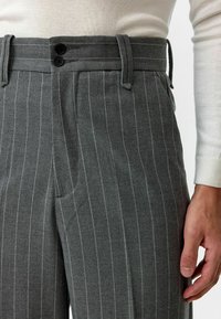 Grijze pinstripe broek met een tailored fit, voorzien van twee zwarte knopen, ceintuurlussen en een textuurstof. Zichtbare zijzak.