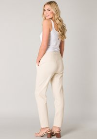 Beige broeken met een taps toelopende pasvorm, elastische taille en achterzakken, gecombineerd met een witte tanktop en beige hakken.