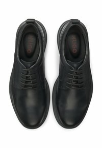 Schwarze Schnürschuhe aus Leder mit abgerundeten Zehen und dicken Sohlen, von oben gesehen, mit "HUGO"-Logo im Inneren der Fersen.