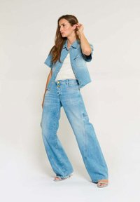 Denim jas en hoge taille, wijde jeans in lichtblauw. De jas heeft korte mouwen; de jeans hebben een knoopsluiting en subtiele stiksels.