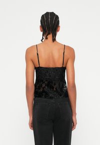 Melnā krekliņa ar caurspīdīgu ziedu audumu, regulējamiem siksniņām, pieguļošs dizains. Saskaņots ar augsta vidukļa melnajām džinsām, gluda tekstūra.