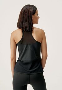 Juodas sportinis tank top'as su permatomu tinkleliu nugarinėje dalyje, su išlenktu kraštu ir subtiliu prekės ženklu centre. Medžiaga yra lygi ir elastinga.
