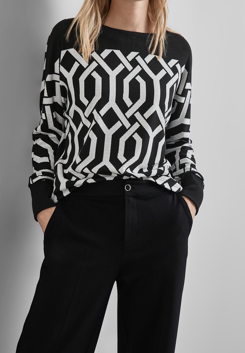 Svart och vit mönstrad tröja med geometrisk design; långa ärmar och ribbade muddar; ihop med svarta byxor med en framficka.