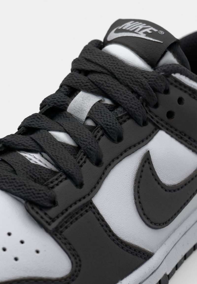 Sneaker Nike bianco e nero con tomaia in pelle texture, cuciture a contrasto e dettagli in pizzo nero piatto.