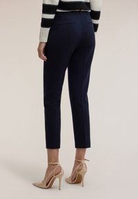 Granatowe, dopasowane spodnie o wąskim kroju, z gładką teksturą i dwoma tylnymi kieszeniami, zestawione z cielistymi szpilkami.