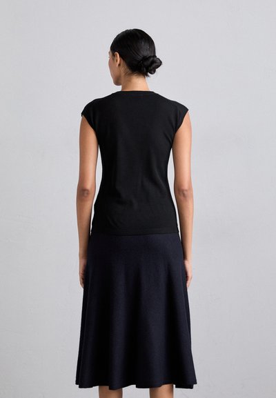 Black sleeveless top with a fitted design and soft texture, paired with a dark navy flared skirt. The outfit has a sleek, minimalist look.