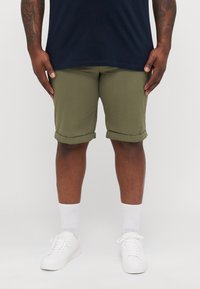 Olive green cuffed shorts in cotton material, paired with white socks and sneakers, worn with a navy shirt, showcasing a relaxed fit.