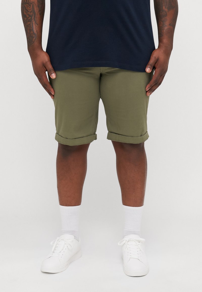 Olive green cuffed shorts in cotton material, paired with white socks and sneakers, worn with a navy shirt, showcasing a relaxed fit.