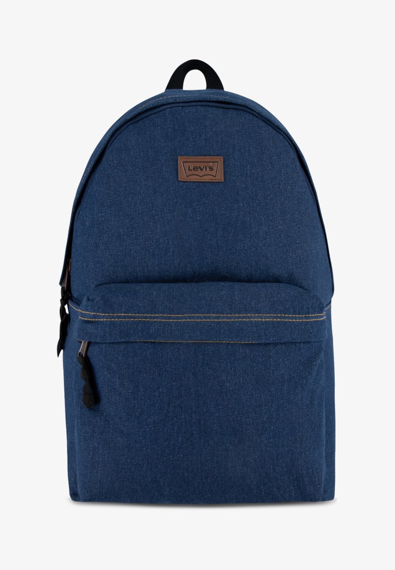 Mochila de denim azul com um topo arredondado, bolso frontal com fecho, etiqueta de logotipo em couro castanho e costura amarela em contraste. Inclui alças ajustáveis.