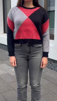 Pulover tricotat roșu, negru și gri cu un model în diamante, guler rotund și manșete cu borduri, purtat cu blugi gri închis.