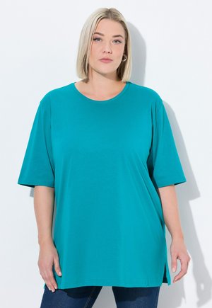 Türkisfarbenes, übergroßes T-Shirt mit Rundhalsausschnitt und kurzen Ärmeln. Besitzt einen seitlichen Schlitz am Saum und ist aus einem glatten, leichten Stoff gefertigt.