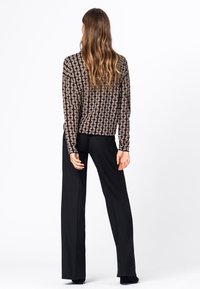 Langærmet top i brun med et geometrisk mønster, parret med sorte vide bukser. Glat tekstur; afslappet pasform. Rent, minimalistisk design.