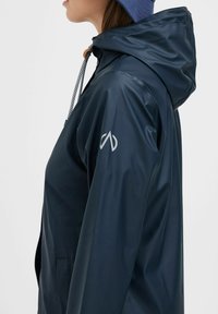 Navy waterproof jacket with a fitted hood, adjustable drawstring, and a silver logo on the left sleeve. Smooth, shiny texture.