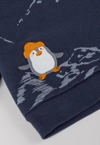 Felpa blu navy con un pinguino ricamato che indossa un cappello arancione, con grafiche di montagne grigie sul davanti e tessuto a trama.