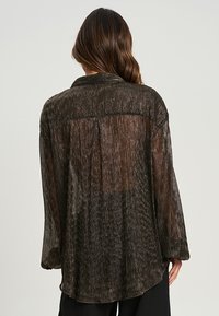Blusa nera trasparente con righe verticali, maniche lunghe e vestibilità ampia. Presenta un colletto classico e una texture morbida.