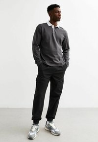 Grijze lange mouwen polo met een witte kraag, gecombineerd met zwarte cargobroeken en grijze sneakers. Casual, ontspannen pasvorm ontwerp en gestructureerde stof.