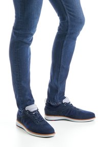 Baskets en maille respirante bleu marine avec accents en daim, semelle blanche et design à lacets, associées à un jean bleu foncé ajusté.