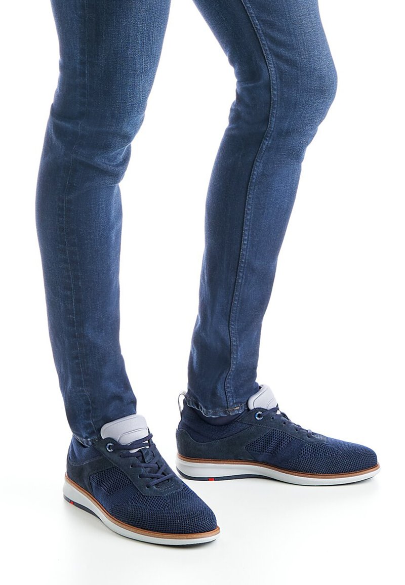 Baskets en maille respirante bleu marine avec accents en daim, semelle blanche et design à lacets, associées à un jean bleu foncé ajusté.