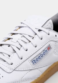 Fehér bőr sneaker, textúrált felülettel, fűzős kialakítással, oldalon lévő logóval és gumitalppal. Finom varrási részletek jellemzik.