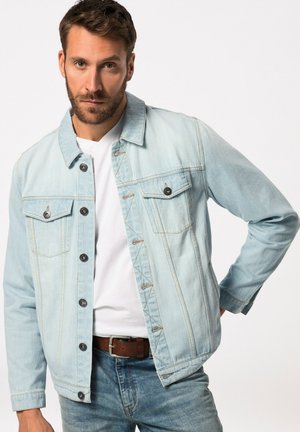 Lys blå denimjakke med knaplukning, to brystlommer og kontrasterende søm. Hvid t-shirt med rund hals, som bæres under.
