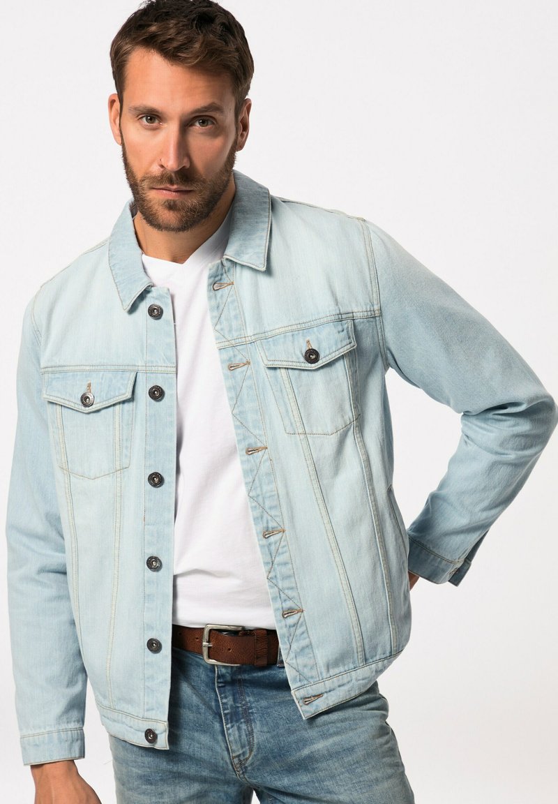 Chaqueta de mezclilla azul claro con botones en el frente, dos bolsillos en el pecho y costuras de contraste. Camiseta blanca de cuello redondo debajo.
