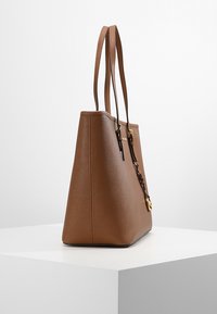 Sac fourre-tout marron avec une finition texturée, deux anses et des accents en métal doré. Présente une forme structurée.