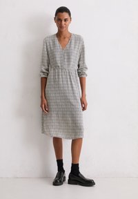 Schwarz-weiß gemustertes Kleid mit V-Ausschnitt, langen Ärmeln und elastischem Bund, kombiniert mit schwarzen Socken und Schuhen.