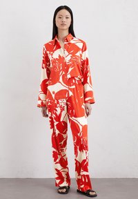 Ensemble léger à motifs floraux rouges et blancs, comprenant une chemise à col et des pantalons avec des manches longues et une taille élastique. Sandales plates.