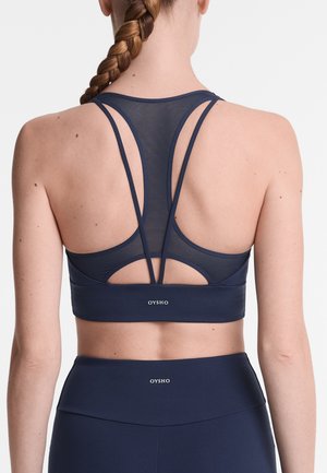 Navy sports bra with mesh detailing, featuring a racerback design, thin straps, and a branded elastic band. Smooth texture and fitted shape.