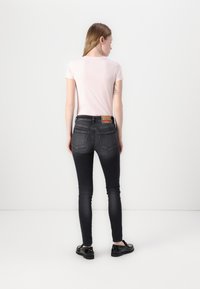 Camiseta ajustada de color rosa claro combinada con unos pantalones ajustados gris oscuro. Los pantalones cuentan con bolsillos traseros y una etiqueta distintiva en la cinturilla. Unos zapatos negros completan el atuendo.