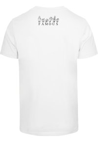 Balts īsām piedurknēm T-krekls ar roku zīmējumiem rindā virs vārda "FAMOUS" tumši melnos burtos uz augšējās daļas mugurā.
