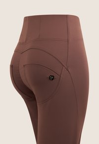 Leggings marroni a vita alta con una texture liscia, caratterizzati da una tasca sul retro con un'accento decorativo in metallo nero e dettagli di cucitura curvi.
