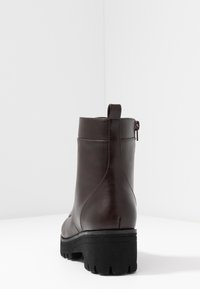 Bottine en cuir marron à finition lisse, fermeture éclair et semelle extérieure noire épaisse. Dotée d'une languette arrière courte pour un enfilage facile.