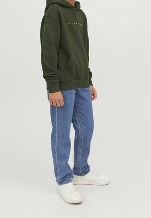 Sweat à capuche vert olive avec une poche devant et un texte blanc, associé à un jean bleu délavé de teinte moyenne et des baskets blanches avec une semelle texturée.