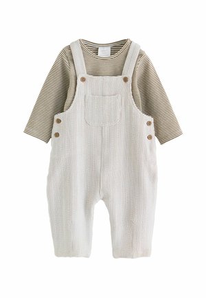 Beiger gerippter Overall mit Holzknöpfen über einem braun-weiß gestreiften Babyshirt mit langen Ärmeln auf weißem Hintergrund.