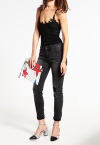 Musta body, jossa on pitsiyksityiskohtia, harmaat kapeat farkut revityillä helmillä, hopeiset läpyskät, ja kuvioitu clutch, jossa on punaisia tähtiä.