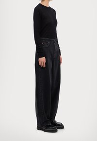 Musta pitkähihaiseksi ylhäältä puettava paita yhdistettynä korkeavyötäröisiin leveälahkeisiin mustiin farkkuihin. Puserossa on läpikuultava tekstuuri, minimalistinen muotoilu ja tasaisten väriensä vuoksi.