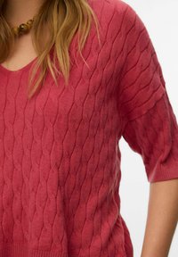Kratek pulover s kratkimi rokavi, izdelan iz pletenine v temno roza barvi z teksturiranim vzorcem kitke. Ima širok V-izrez in rebraste manšete.